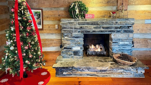 A cozy room with a stone fireplace, a Christmas tree, and a 'Joy' sign.