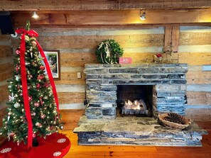 Een knus vertrek met een stenen openhaard, een kerstboom en een bord met de tekst 'Joy'.