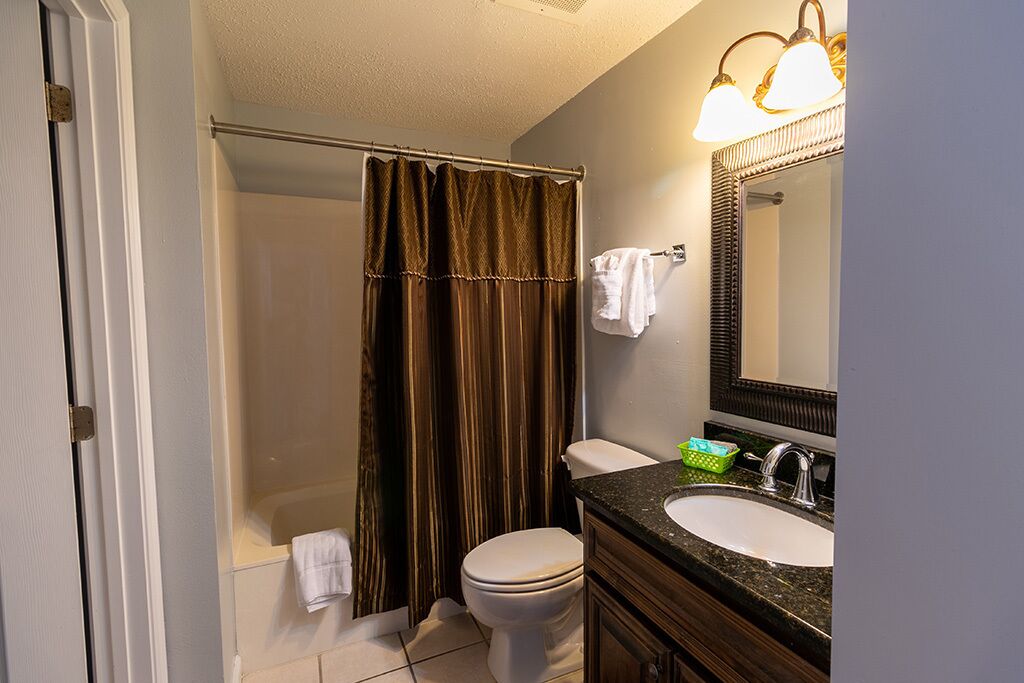 A bathroom with a shower, toilet, sink, and mirror.