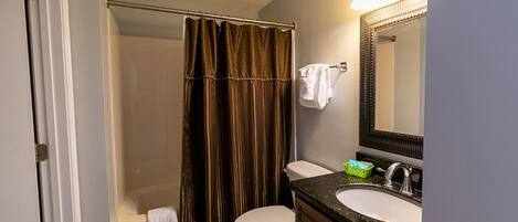 A bathroom with a shower, toilet, sink, and mirror.