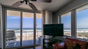 A living room with a large TV, a leather couch, and a view of the beach through a sliding glass door. - FREE Beach Chairs, GULF FRONT, Common Pool/Hot Tub, VIEWS!, Wrap around balcony (Navarre)