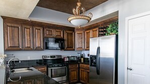 A modern kitchen with wooden cabinets, stainless steel appliances, and a decorative ceiling light. - FREE Beach Chairs, GULF FRONT, Common Pool/Hot Tub, VIEWS!, Wrap around balcony (Navarre)
