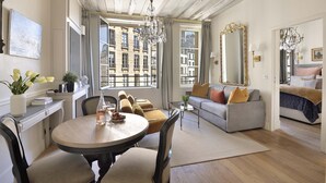 Un salon bien éclairé comprenant un coin repas, un canapé, un grand miroir et une vue sur la ville grâce à de grandes fenêtres.