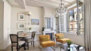 Un coin repas avec une table ronde, des chaises et un lustre. Une fenêtre offre une vue sur les bâtiments environnants.