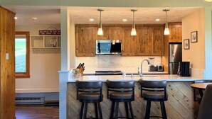 Une cuisine moderne avec des meubles en bois, un réfrigérateur en acier inoxydable, un four à micro-ondes et un coin bar avec des tabourets.