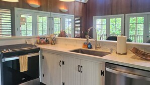 A kitchen with wooden cabinets, a stainless steel dishwasher, and a large island with a sink. - Beautiful Plumeria Cottage-Anini Beach Plantation Style Home  (Anini Beach)