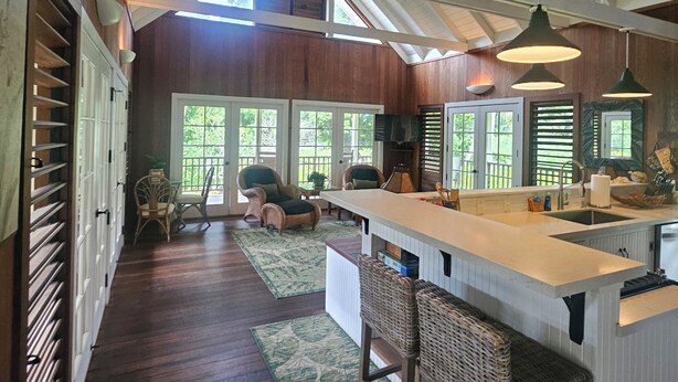 A spacious kitchen with a high ceiling, large windows, and a central island with bar stools. - Beautiful Plumeria Cottage-Anini Beach Plantation Style Home  (Anini Beach)
