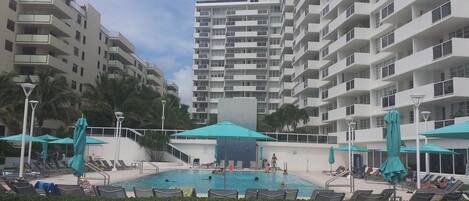 A swimming pool area with lounge chairs and umbrellas, surrounded by high-rise residential buildings.