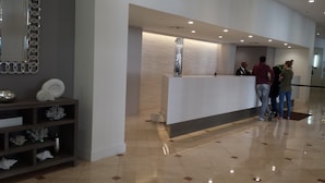 A reception area with a white reception desk, a decorative shelf with shells, and a polished floor. - SOBE ~ ART DECO DISTRICT ~ SOUTH BEACH ~ RITZ CARLTON       Condo on the Water (Miami Beach)