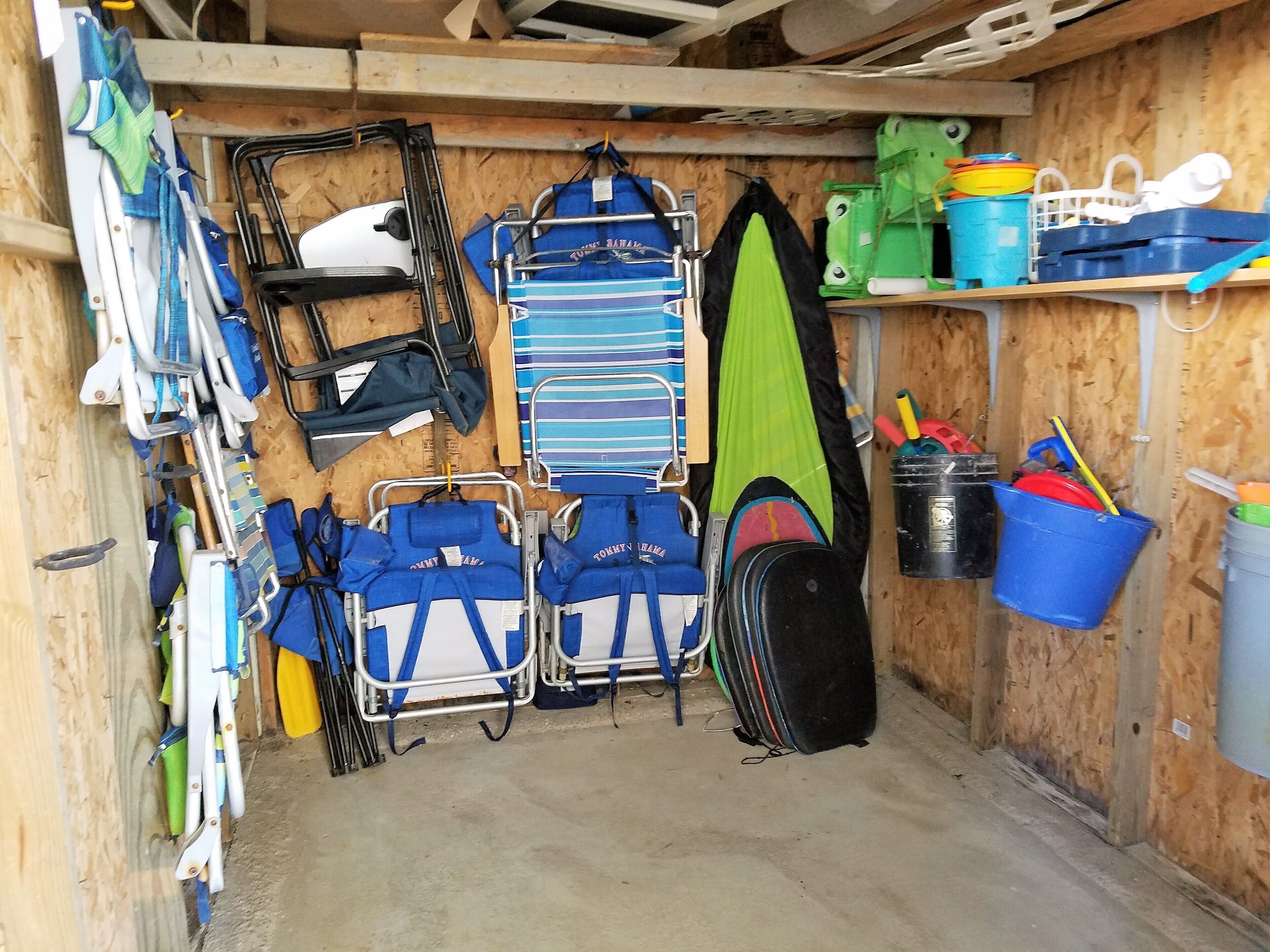 Un espace de rangement doté d’étagères où sont entreposés divers objets, comme des sacs, une planche de surf verte et des seaux.