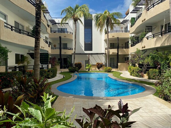 A swimming pool surrounded by lush greenery and multi-story buildings with balconies.