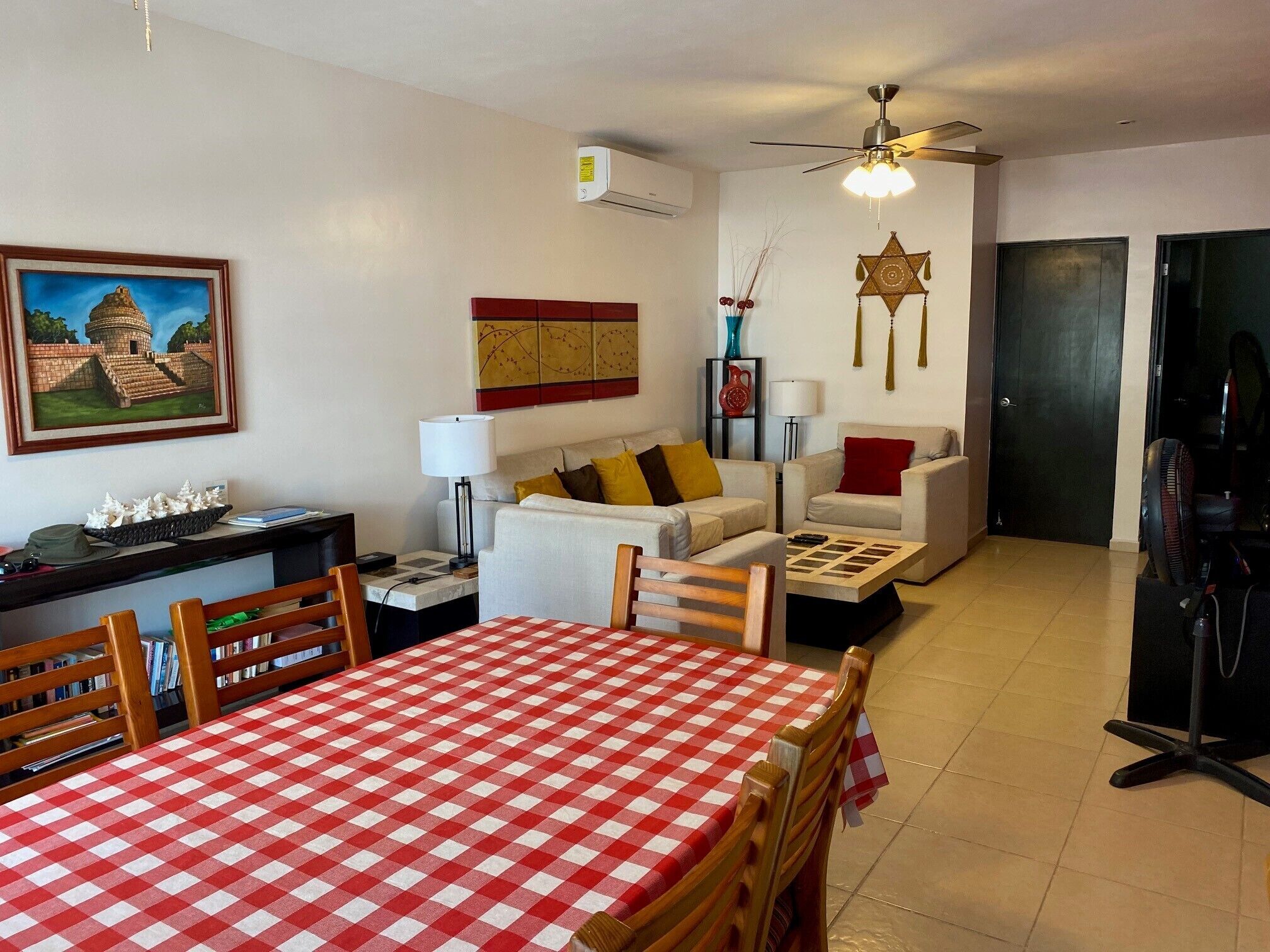Un salon avec une table à carreaux, deux canapés, un ventilateur de plafond et un tableau représentant une pyramide.