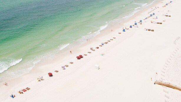 A beach with a long stretch of sand, a few umbrellas, and a wooden fence along the water's edge. - 3BR/3BA - Beach, pool, lagoon front and MORE!  (Gulf Shores)