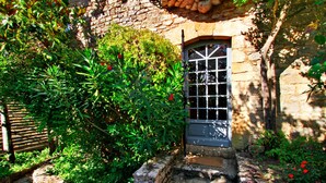 Un edificio in pietra con una finestra e un portone, immerso nel verde e con un vialetto in pietra.