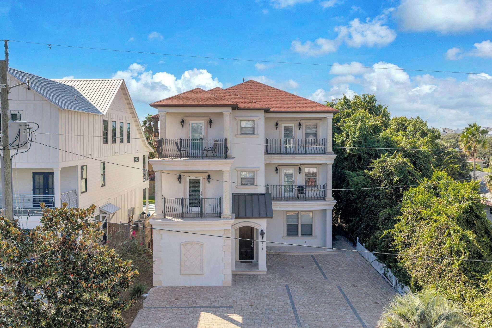 A multi-story residential building with a red-tiled roof, a front entrance, and a small front yard.