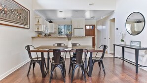 Un comedor con una mesa y sillas de madera, una cocina al fondo y una obra de arte grande enmarcada en la pared.