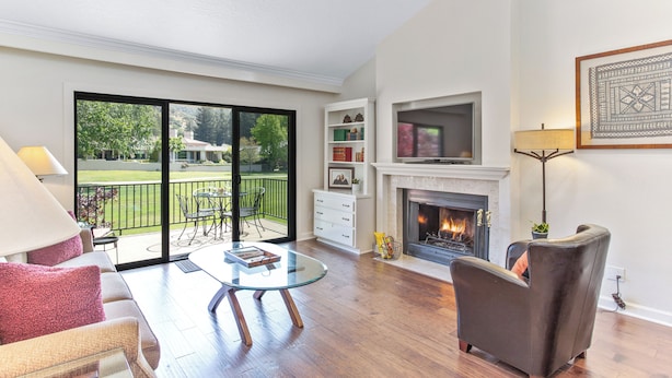 Amplia sala de estar con una mesa de centro de vidrio, un sillón de cuero, chimenea y un balcón con mobiliario exterior.