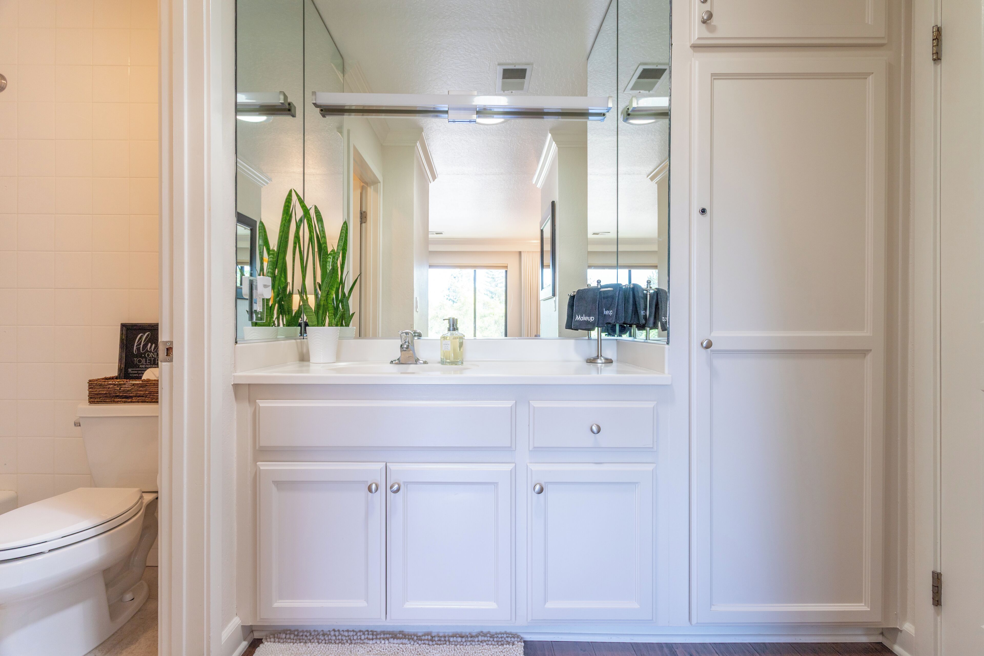 A modern bathroom with white cabinetry, a large mirror, and a toilet.