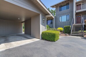 Un bâtiment à deux étages doté d’un espace de stationnement couvert et d’un petit jardin agrémenté d’arbustes.