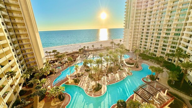 A resort with a central pool, a beach, and high-rise buildings. - Happy Hours@Shores of Panama | Beachfront Resort Pools, Hot Tub & Tiki Bar (Panama City Beach)