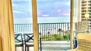 A room with a view of the beach and ocean, a round table, and a sofa with a patterned cushion. - Happy Hours@Shores of Panama | Beachfront Resort Pools, Hot Tub & Tiki Bar (Panama City Beach)