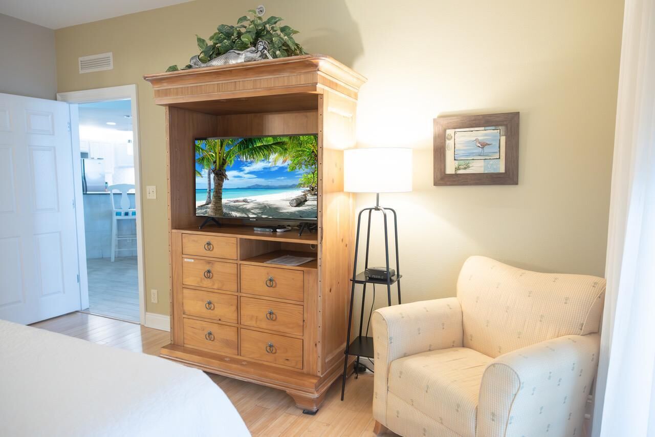 Habitación de hotel con un armario de madera, televisor, lámpara y un cuadro en la pared.