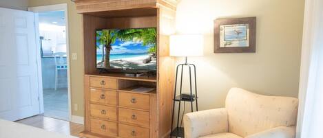 Habitación de hotel con un armario de madera, televisor, lámpara y un cuadro en la pared.