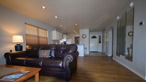 A spacious living room with a leather sofa, wooden coffee table, and a lamp. A hallway leads to a kitchen and dining area. - Center of Town-The Greens at Thousand Hills-2 Comfy Kings-Netflix-PS4-Updated (Branson)