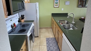 Eine kleine Küche mit Holzausstattung, einer Mikrowelle, einem Kühlschrank, einem Spülbecken und einem gemusterten Teppich.