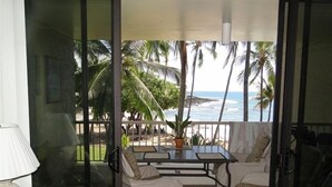 Ein Balkon mit Tisch und Stühlen, der Blick auf einen Strand mit Palmen und dem Meer freigibt.
