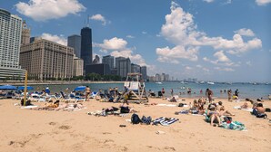 A beach with people sunbathing and swimming, a lifeguard tower, and a city skyline in the background. - 2-Story Penthouse Views, Fireplace, Pool, Gym (Chicago)