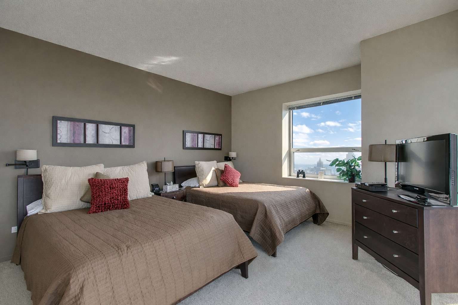 A hotel room with two beds, a TV, a dresser, and a window with a city view.