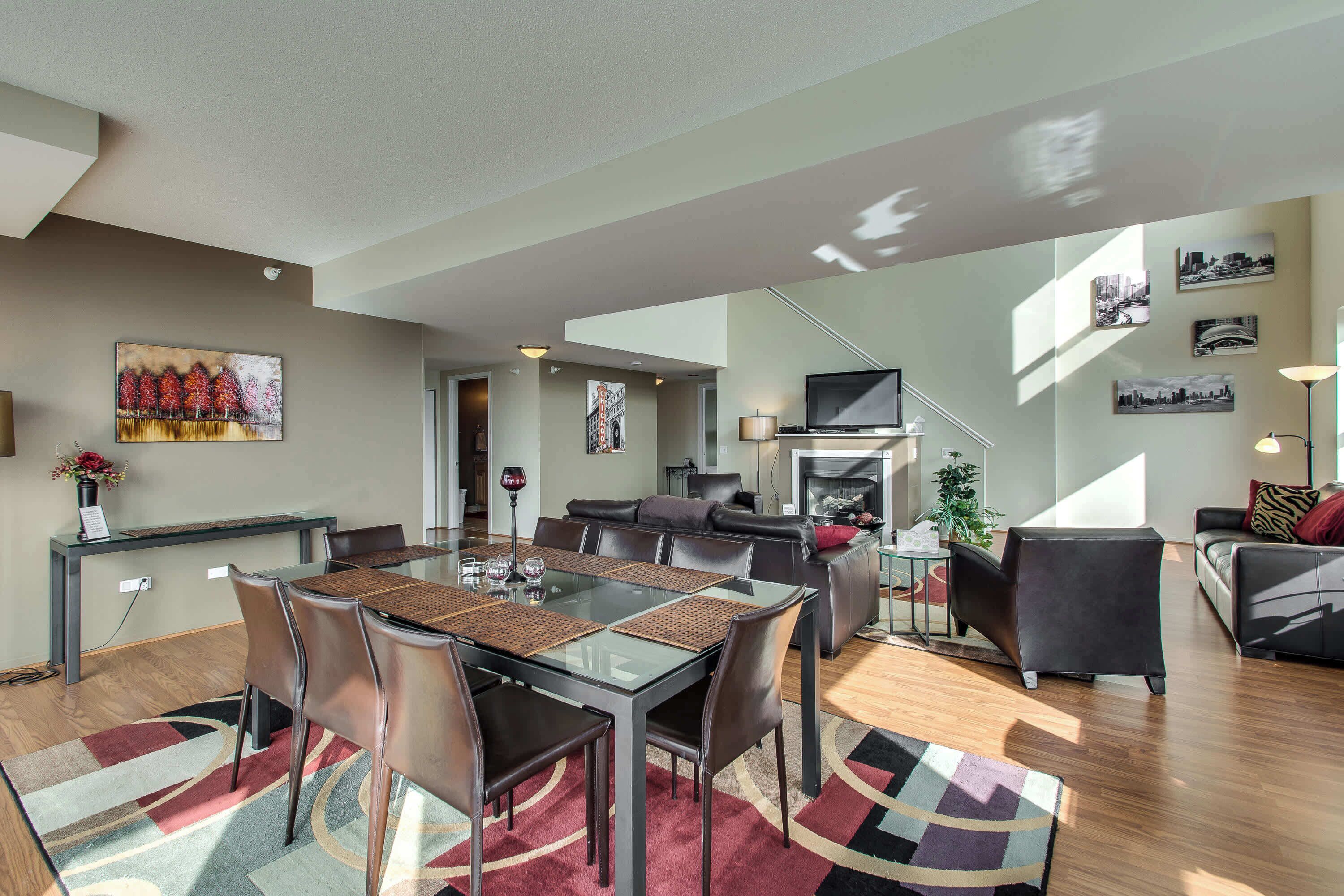 A modern living room with a dining area, a fireplace, and a staircase leading to another level.