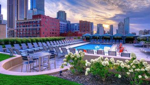 A rooftop pool area with lounge chairs and umbrellas, surrounded by city buildings and a sunset sky. - 2-Story Penthouse Views, Fireplace, Pool, Gym (Chicago)