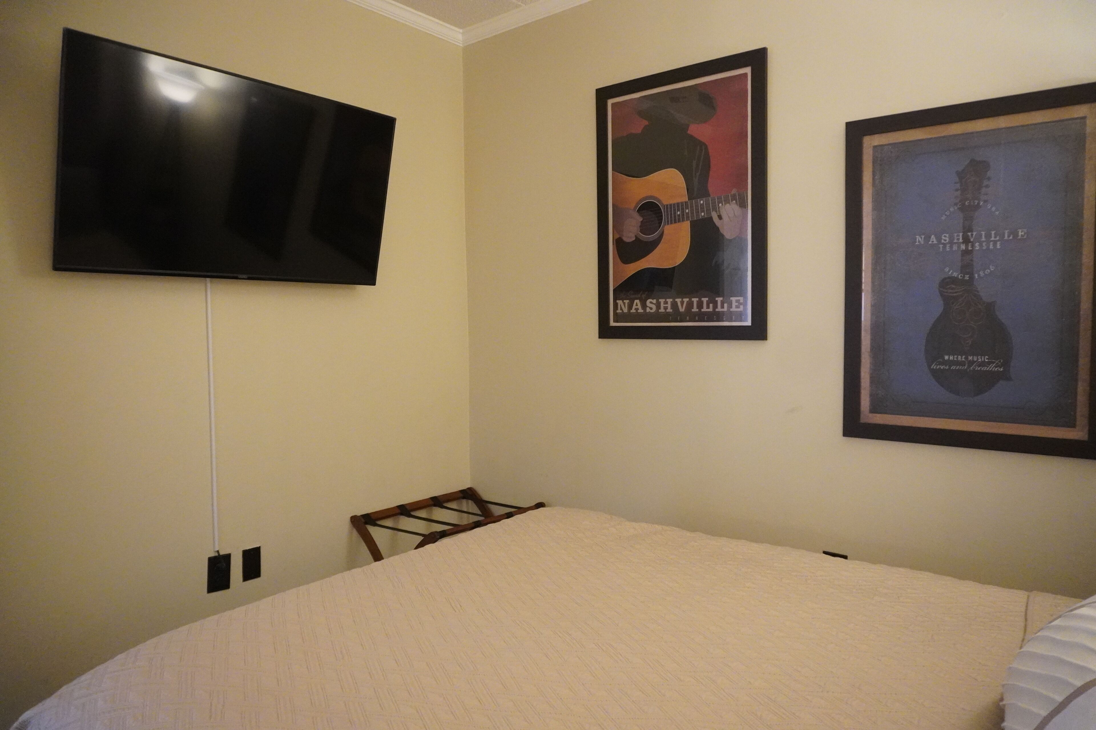 Ein Schlafzimmer mit einem Bett, einem Wand-Fernseher und zwei gerahmten Postern an der Wand.