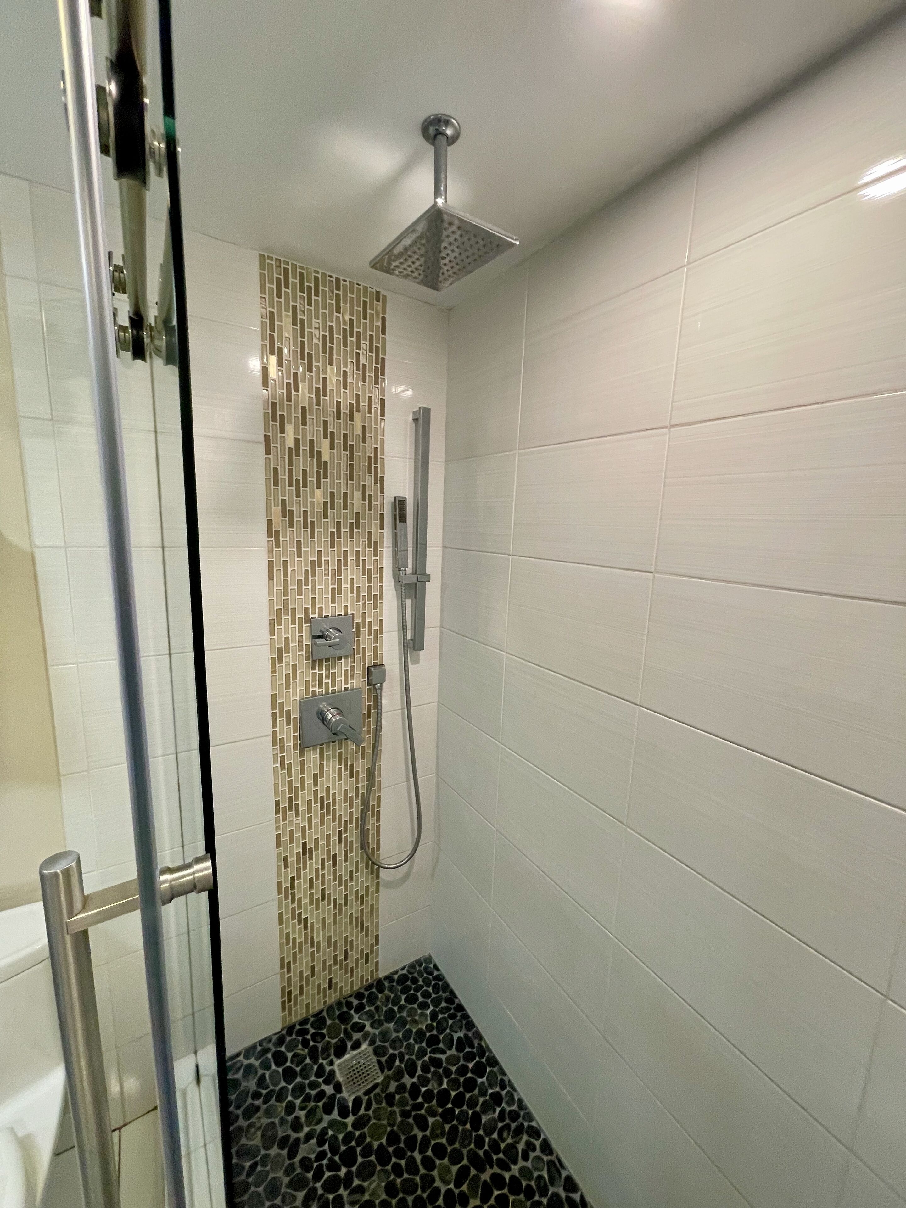 A modern shower with a square showerhead, a handheld showerhead, and a control panel.