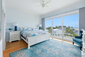 Primary bedroom with white wood bed, coastal bedding, blue area rug, and sliding glass doors overlooking palm trees. - Luxury townhome steps away from Siesta Key Village and Beach! (Siesta Key)