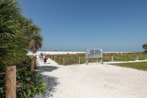 Un sentiero sulla spiaggia che conduce verso l'oceano, con un segnale che indica un evento in programma.