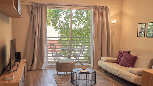 Een moderne woonkamer met een bank, salontafel, televisie en een balkon met tuinmeubilair.