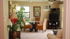 Una sala de estar con una mesa de comedor, sillas, un ventilador de techo, un televisor y una planta grande.