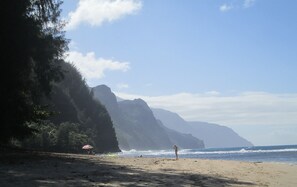 A beach with a person standing, a colorful umbrella, and a mountain in the background.