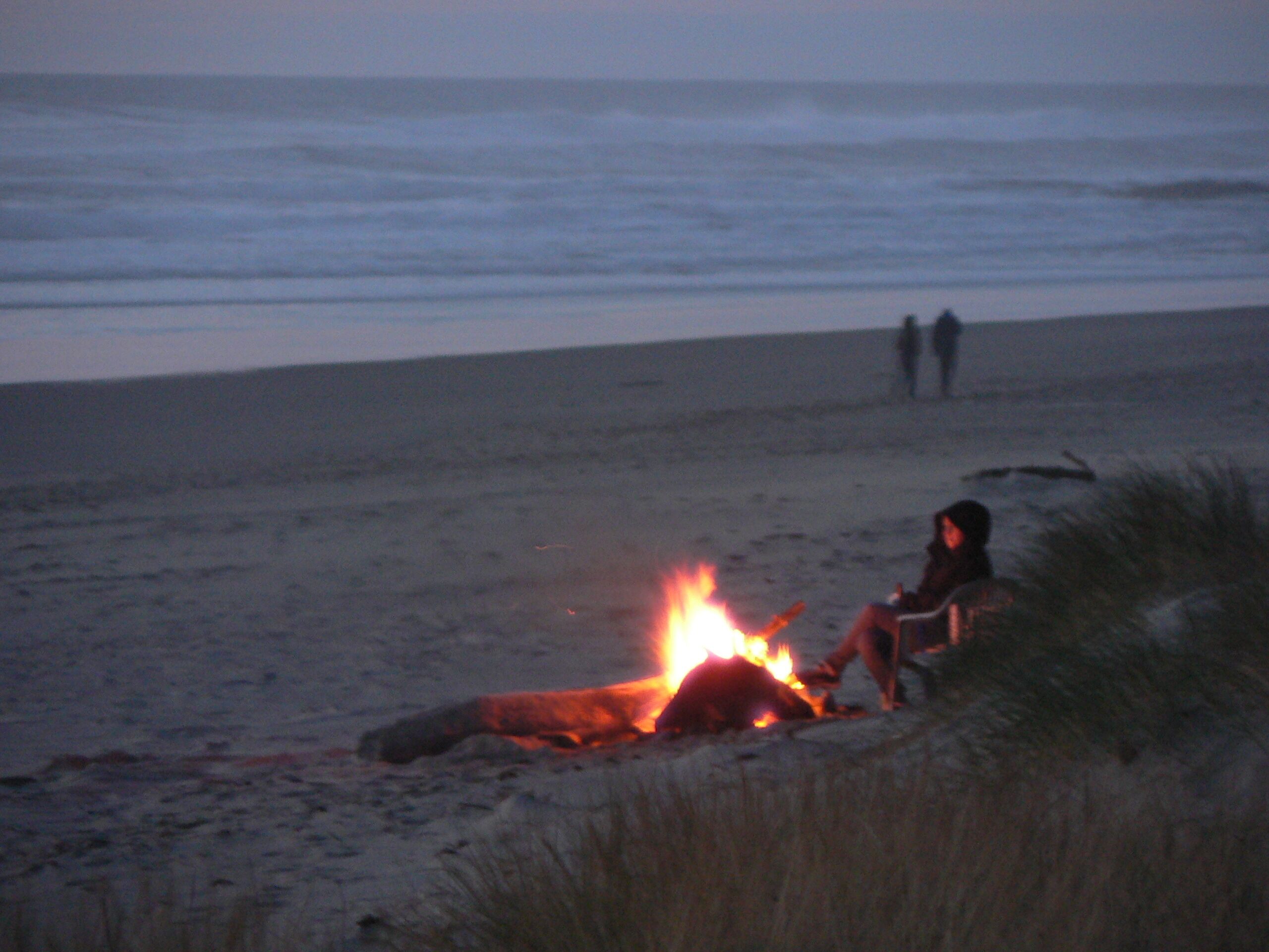 A beach scene with a fire and two people in the background.