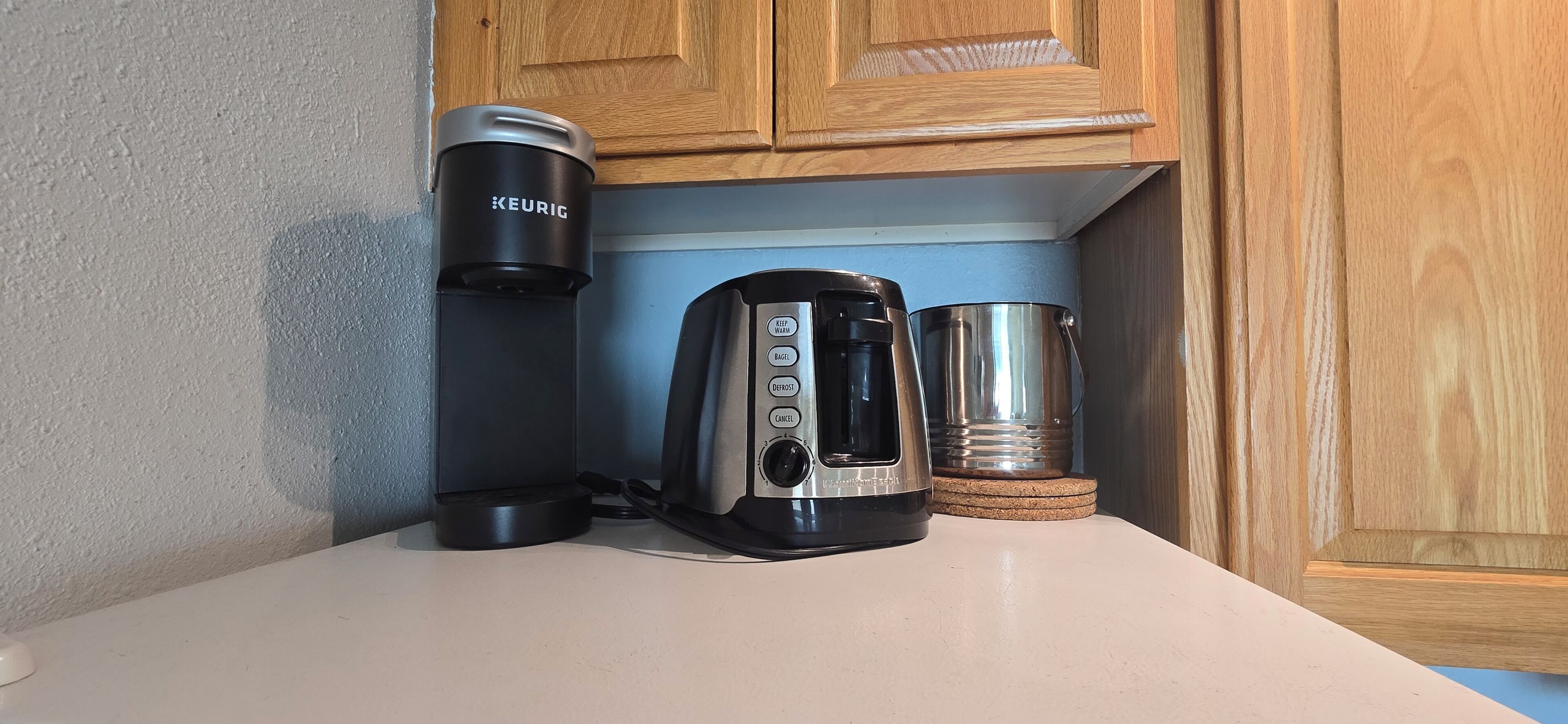 Una cafetera, un dispensador de cápsulas de café Keurig y una taza de acero inoxidable sobre una encimera de cocina.