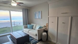 Una sala de estar con un sofá, un reposapiés y vista al océano a través de ventanas grandes.