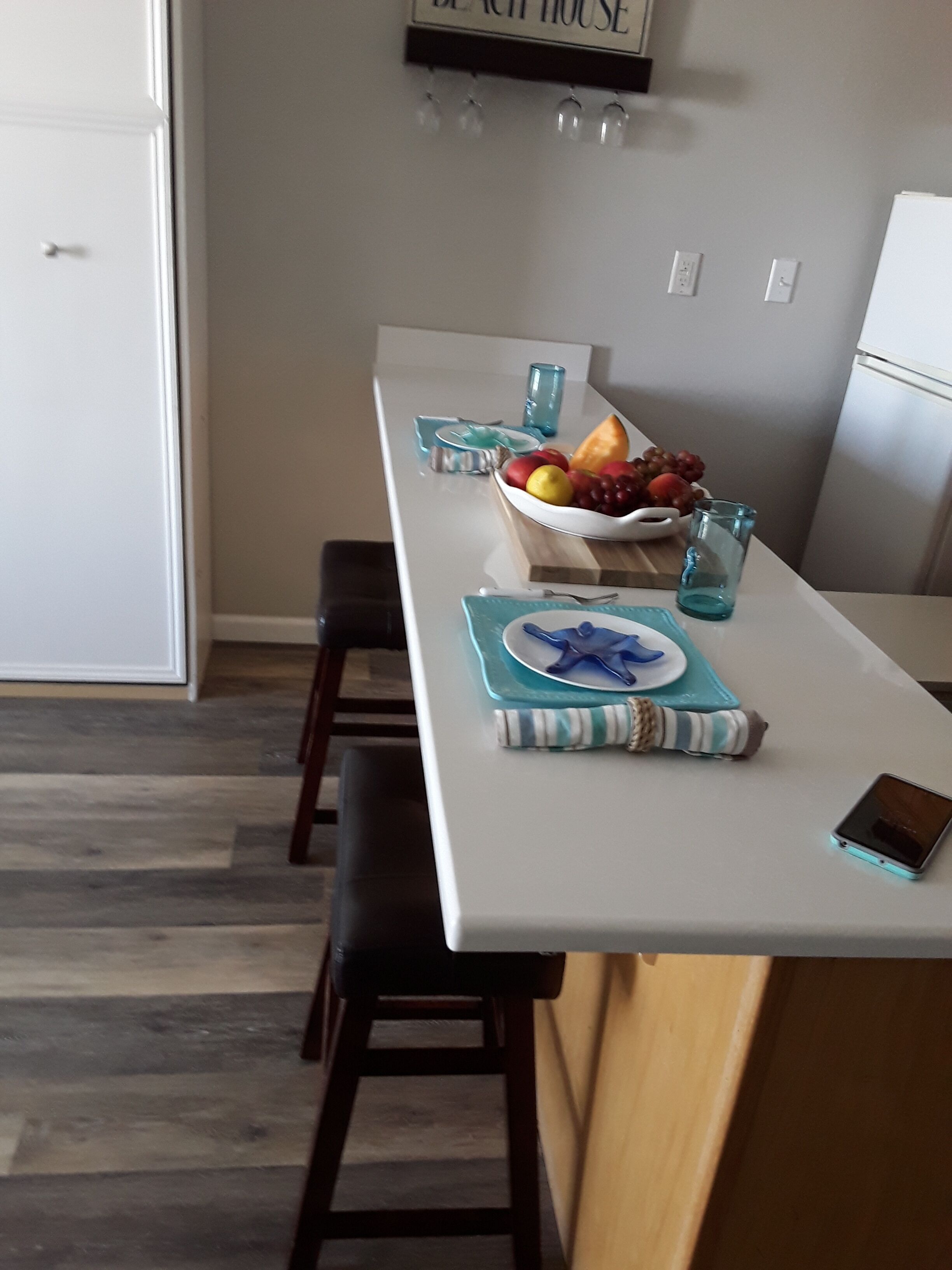 Ett modernt kök med en vit bänkskiva, en skål med frukt och en smartphone på bordet.