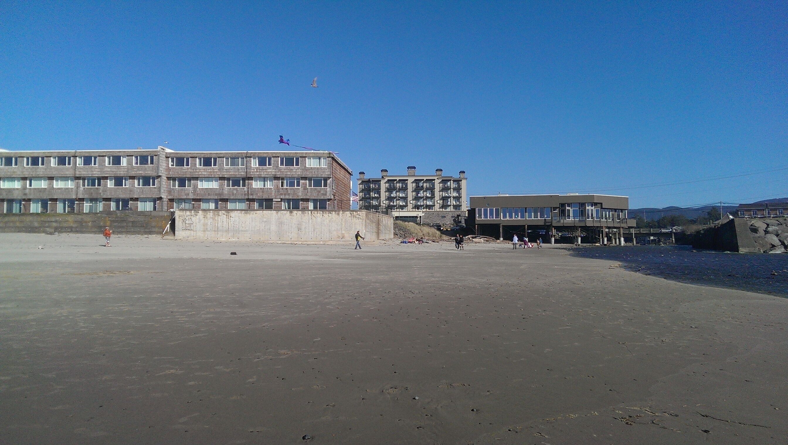 A beach with a large building, a pier, and a clear sky.