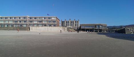 En strand med en stor byggnad, en pir och en klar himmel.