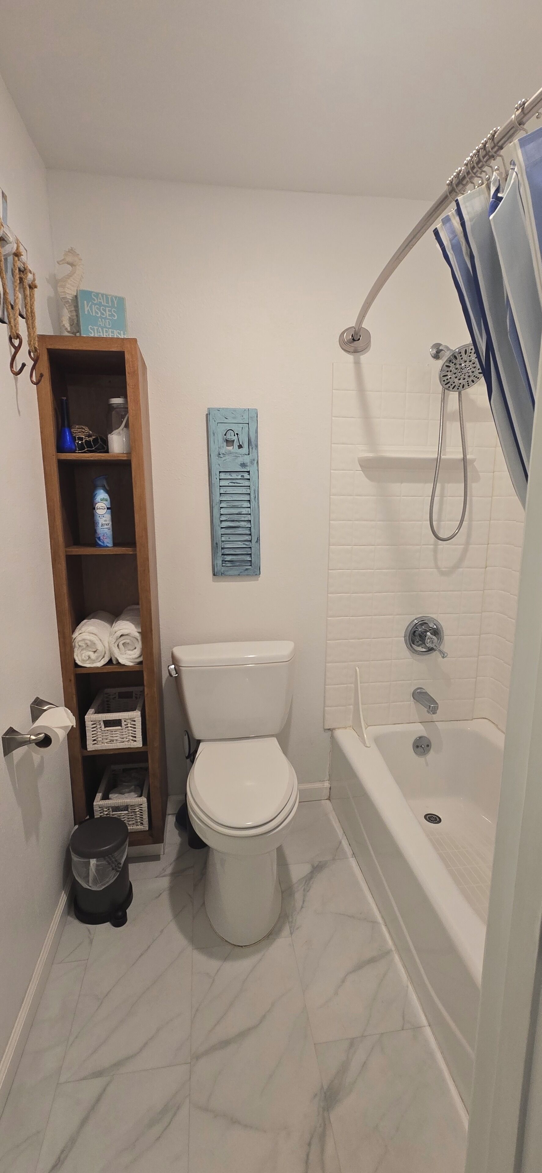 A bathroom with a toilet, a shower, a wooden shelf with towels, and a blue sign.