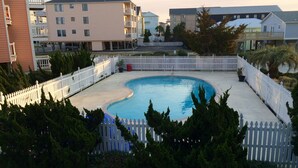 En swimmingpool omgivet af et hvidt stakittet hegn, med bygninger i baggrunden.