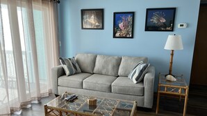 En stue med en grå sofa, to billeder i rammer, et glasbord, en lampe og en stol.